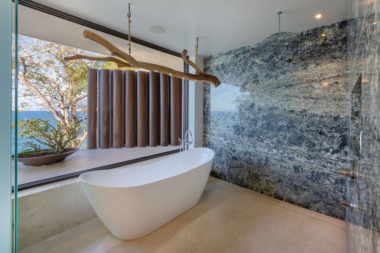 Luxury soaking tub with ocean view, driftwood sculpture and blue stone wall