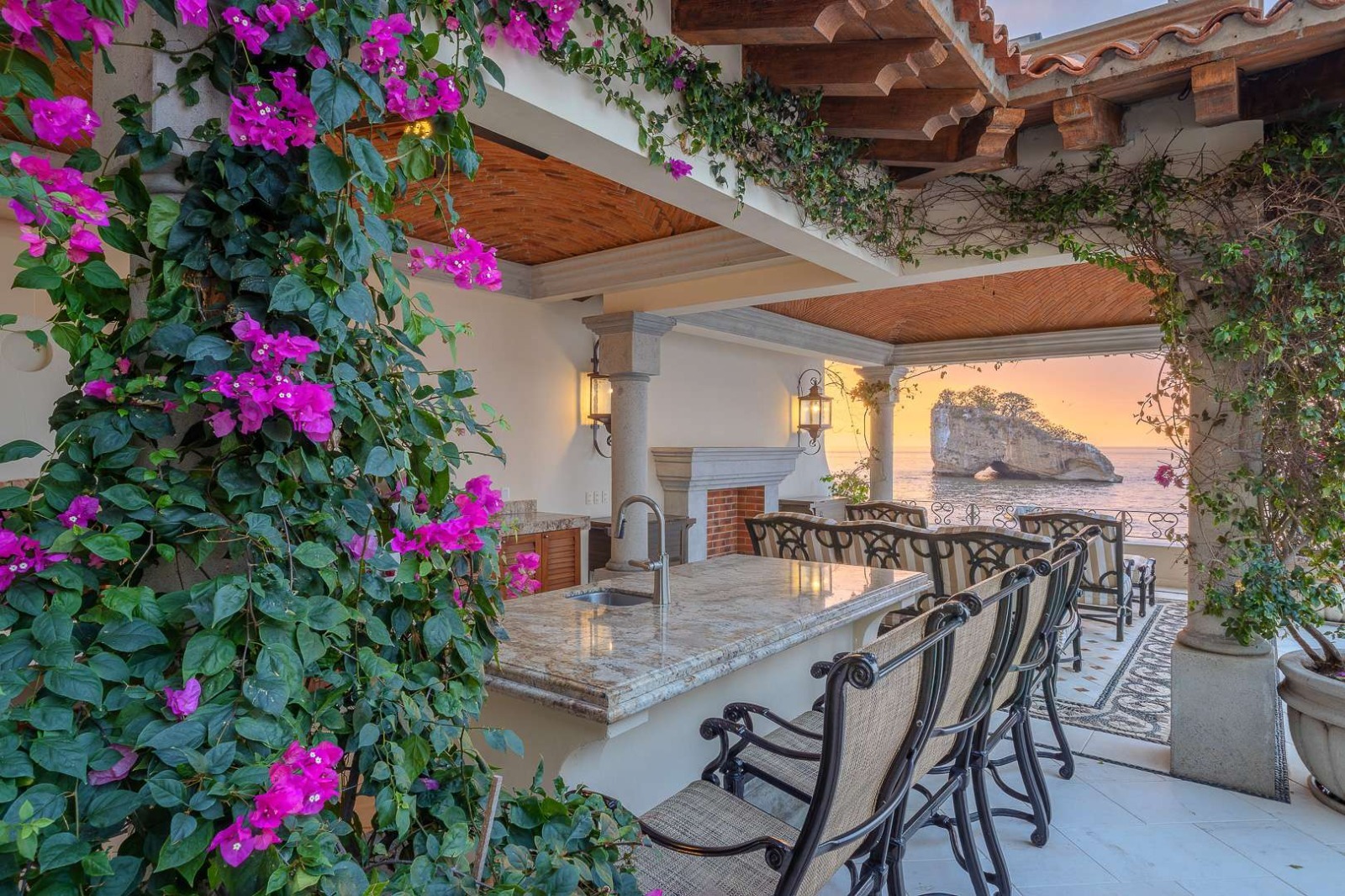 Bougainvillea-draped terrace at sunset with ocean rock formation view