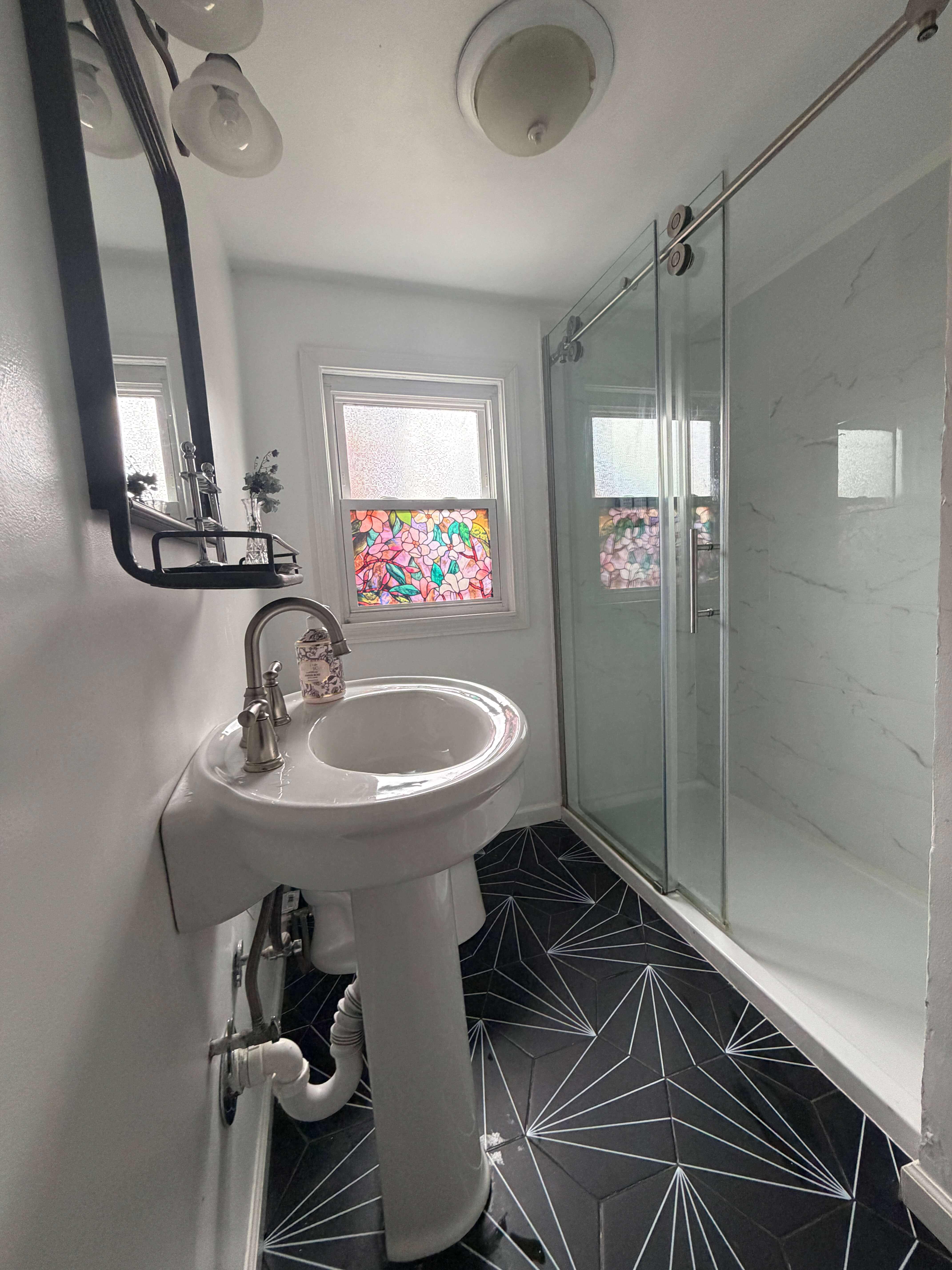 Bathroom after — black geometric tile, glass shower enclosure, pedestal sink