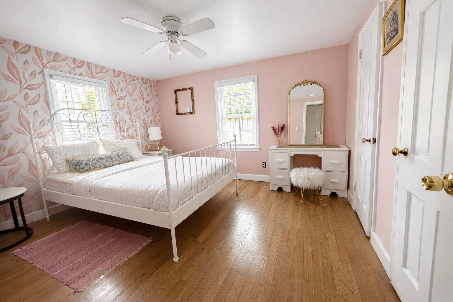 Bedroom after — botanical wallpaper, white iron bed, gold vanity mirror, hardwood floors
