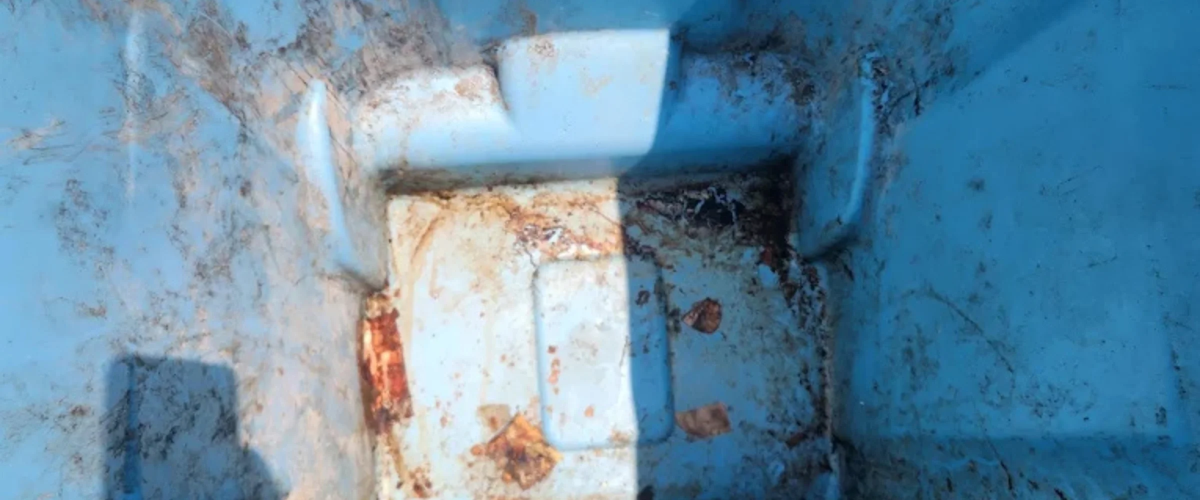 Inside a dirty blue recycling bin with liquid and debris at the bottom, viewed from above.