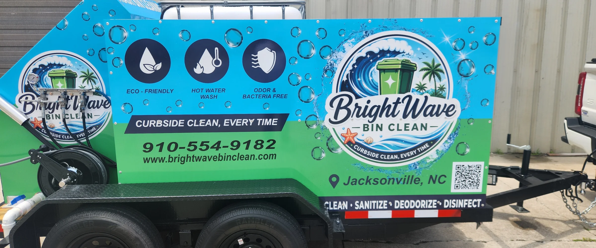 A Bright Wave Bin Clean service trailer, green and blue, hitched to a white pickup truck on a residential street.