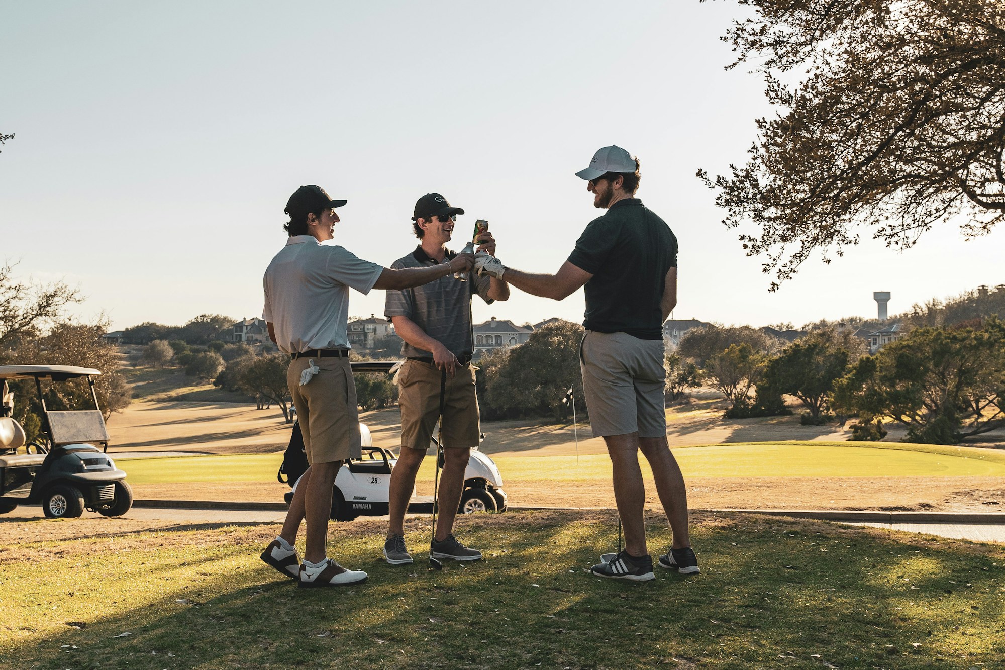 Three friends raising a drink on the course at golden hour