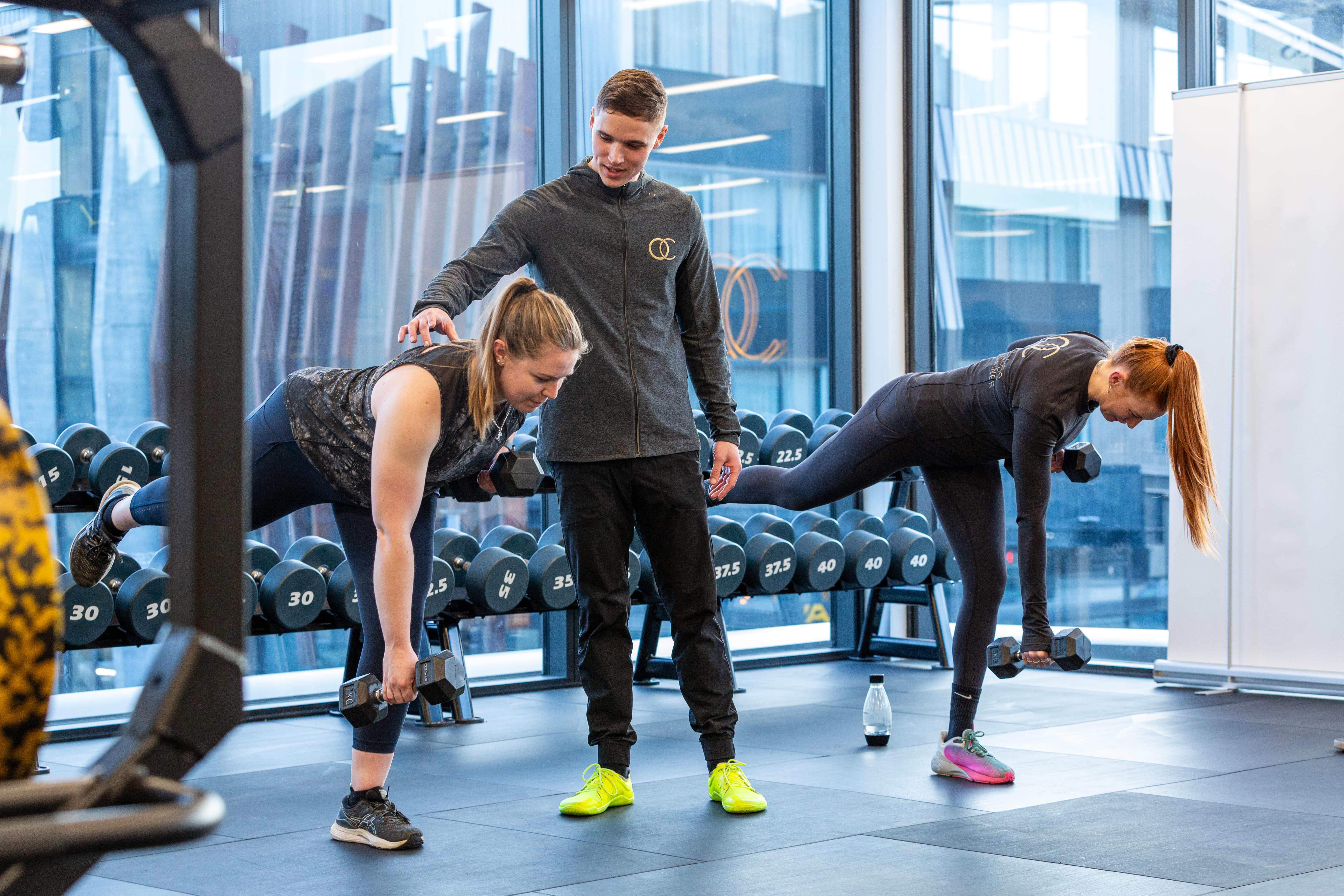 Coach guiding two members through a kettlebell exercise in a small group session at OC Health Clubs