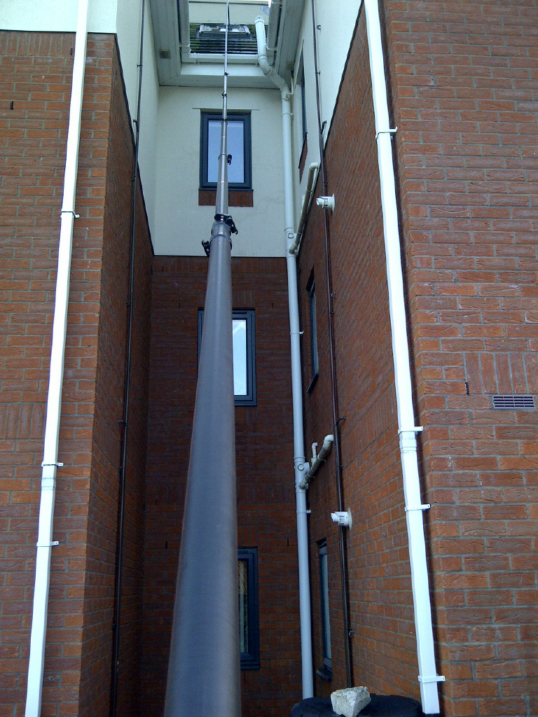 Water-fed pole and cleaning head reaching the upper window between two brick buildings