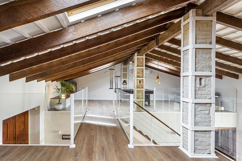 Interior reformado en Godella con altillo metálico y vigas de madera bajo la cubierta