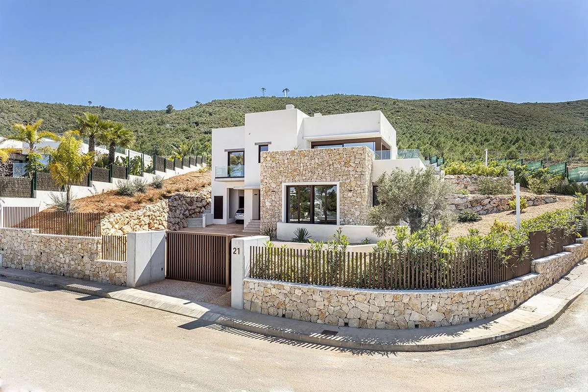 Casa Turna vista desde la calle: villa blanca de dos alturas escalonada sobre la pendiente, con muros de piedra y el Montgó al fondo