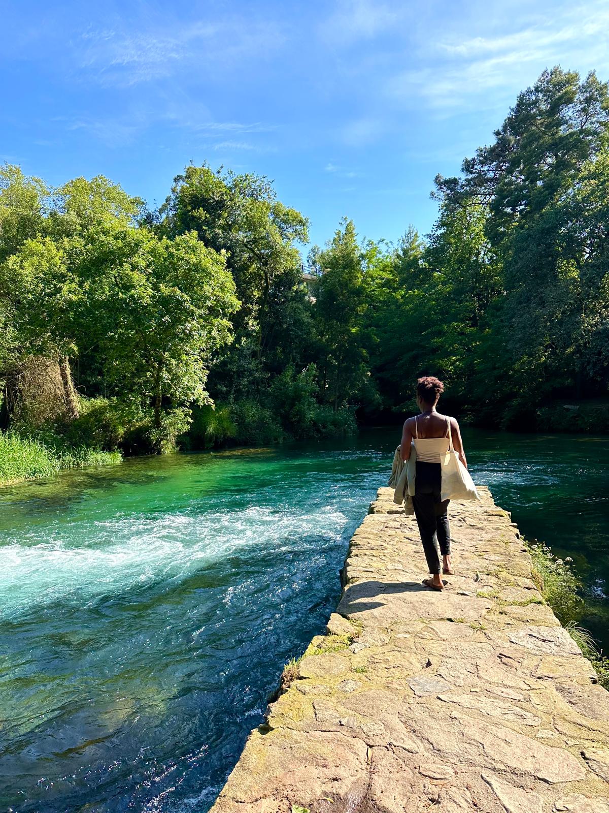 A woman walking a stone weir over a green river