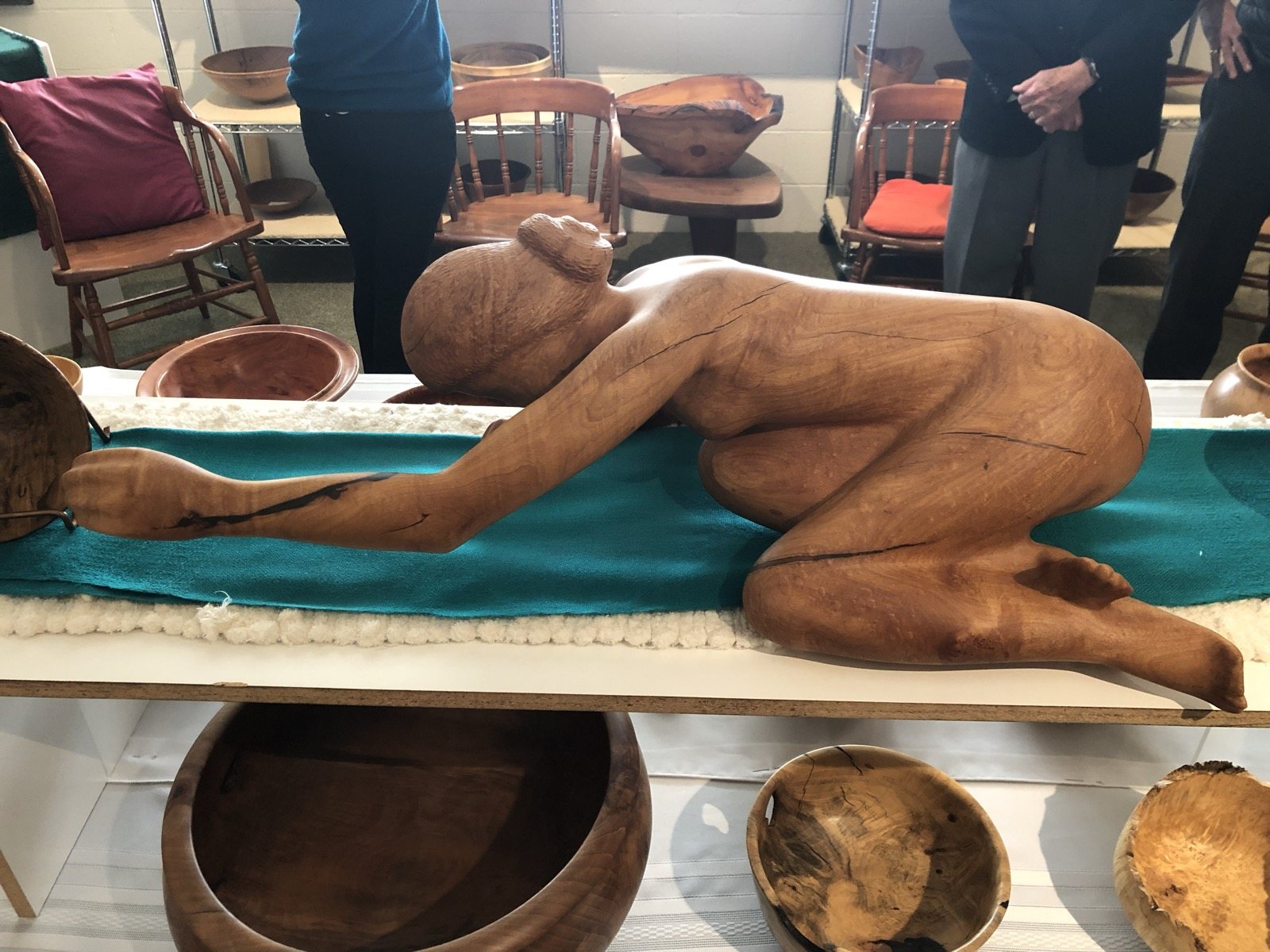 Carved human figure displayed among wood artwork in a studio