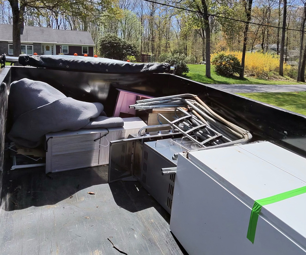 Junk removal truck loaded with mattresses, lumber, a crib, and furniture during a residential property cleanout