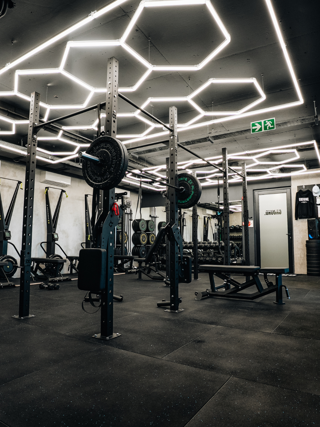 GROUND weight room with squat racks and hexagonal ceiling lights