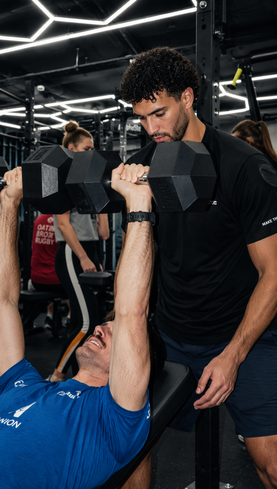 A GROUND coach spotting a member during a dumbbell bench press