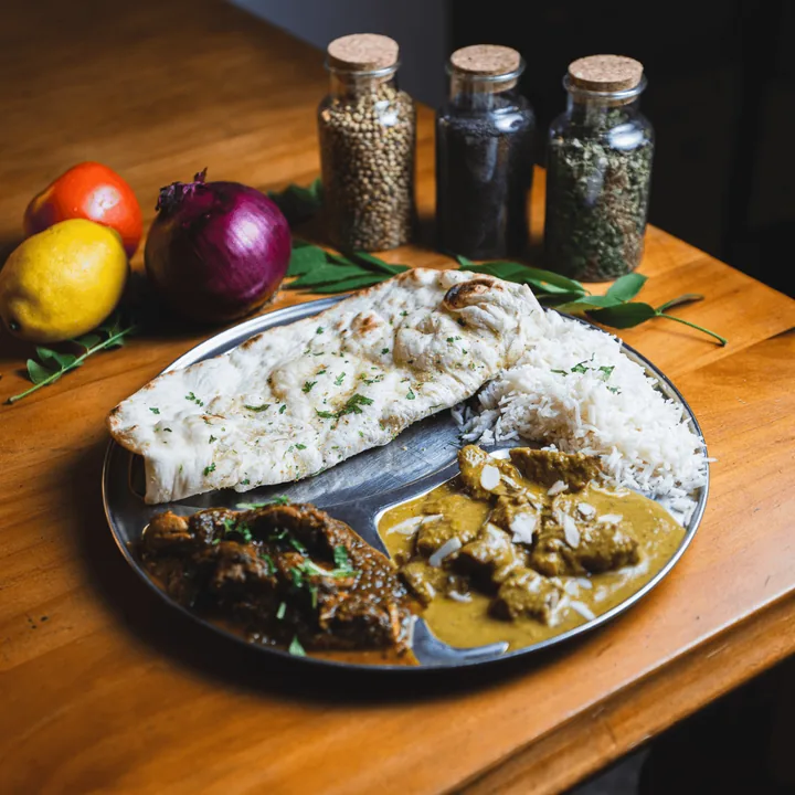 Plate of naan, lamb curry and rice with spice jars