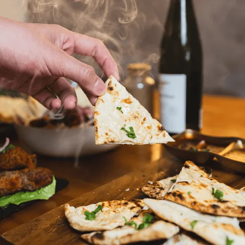 Hand tearing garlic naan with steam rising
