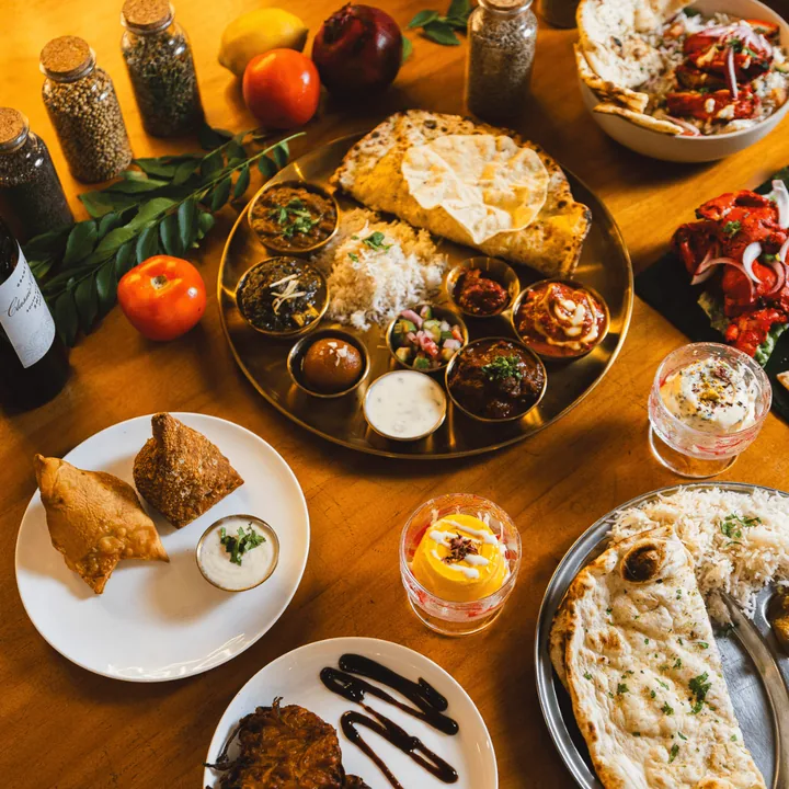 Top-down feast table with samosas, thali, naan and kulfi