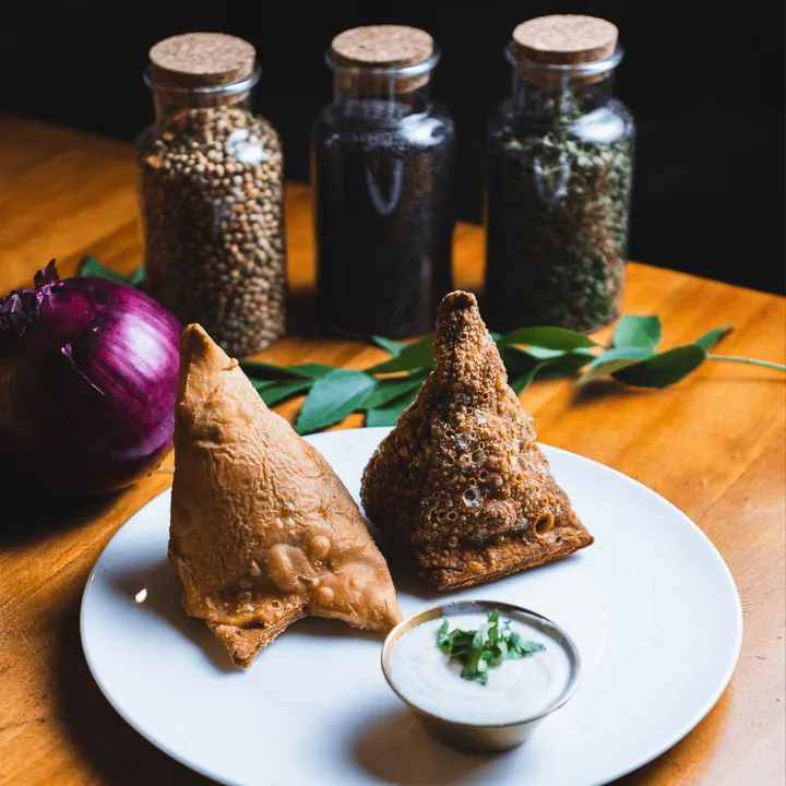Two hand-made samosas with raita and spice jars