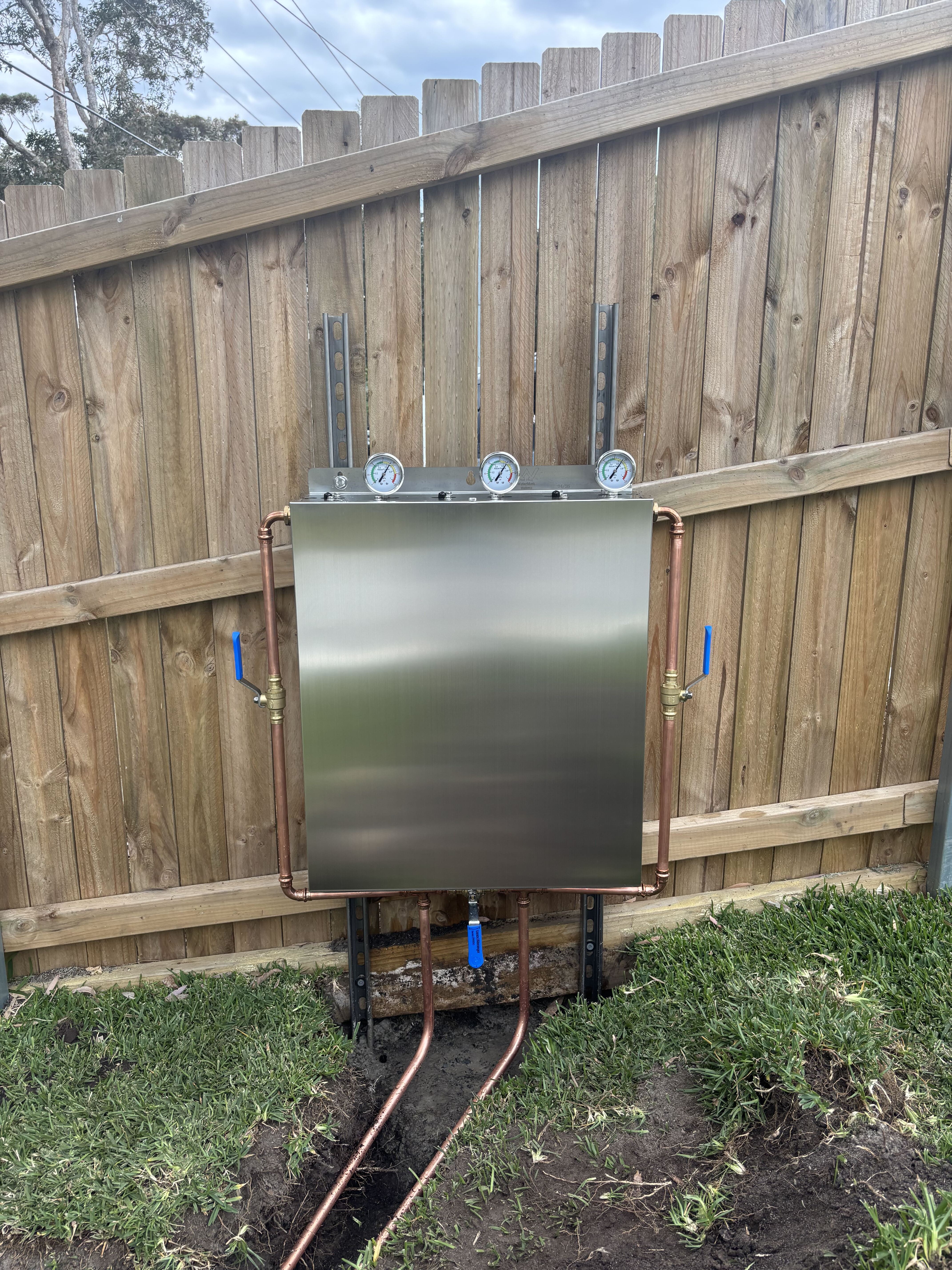Stainless filtration enclosure with copper pipework against timber fence