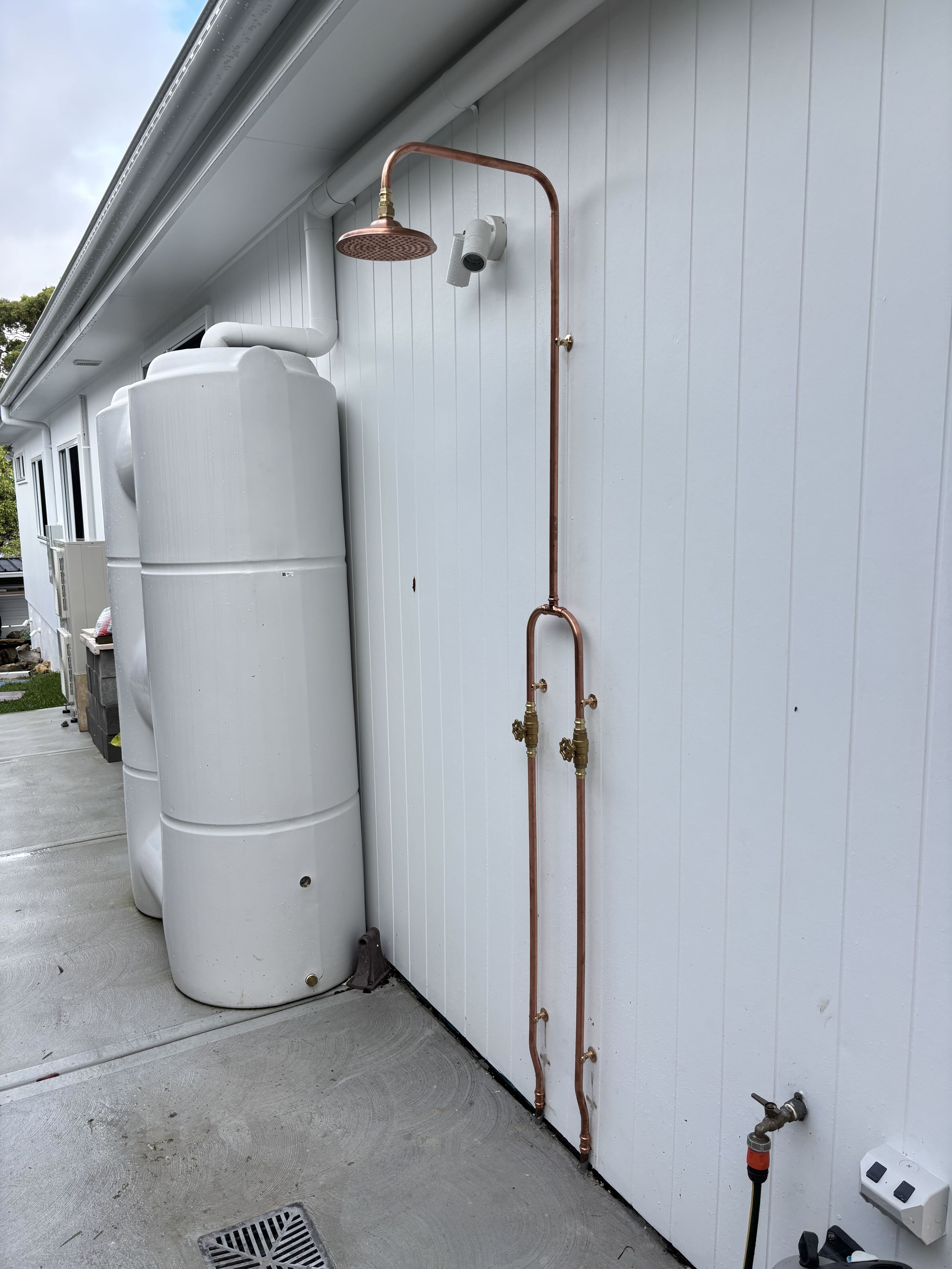 Copper outdoor shower on white weatherboard wall
