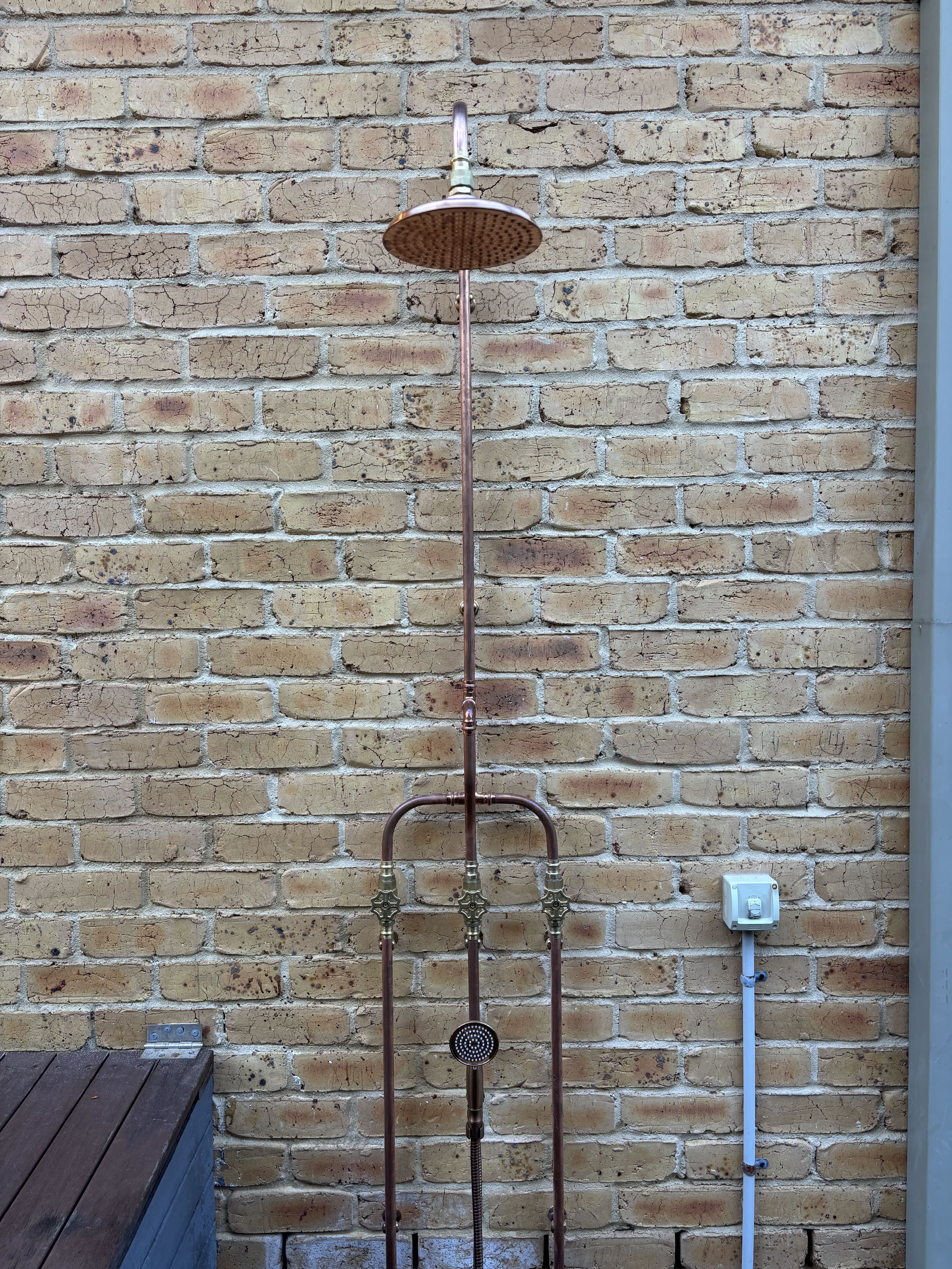 Copper outdoor shower on brick wall