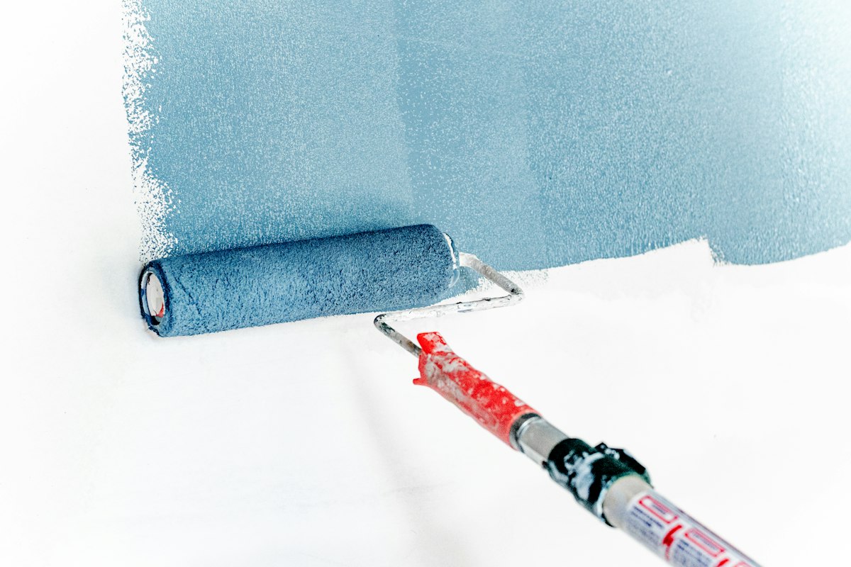 A paint roller rolling fresh paint onto a white wall