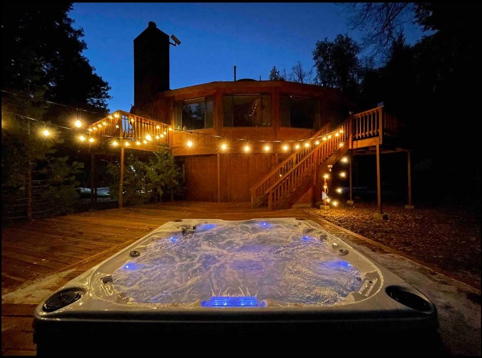 Cabin deck and hot tub under string lights at night