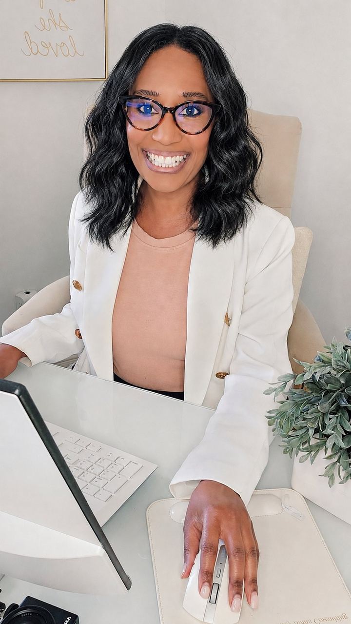 Ashley Binns smiling at her desk in a white blazer