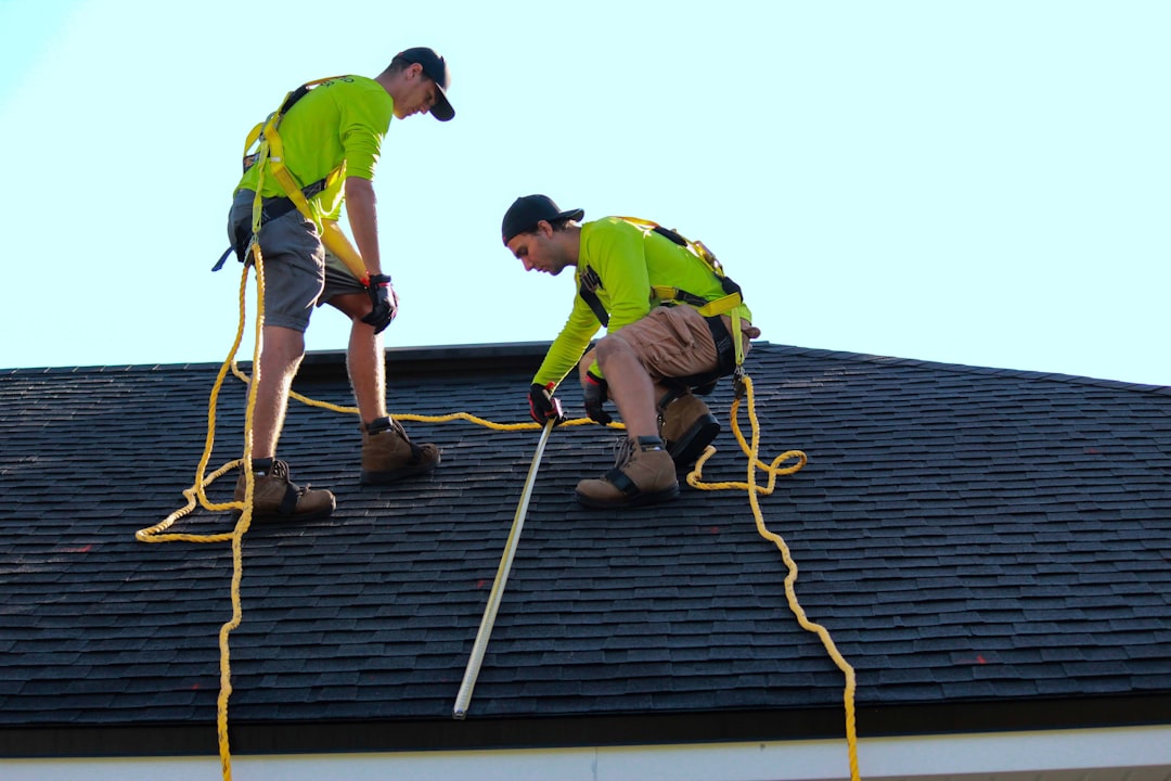 Two roofers installing shingles against blue sky