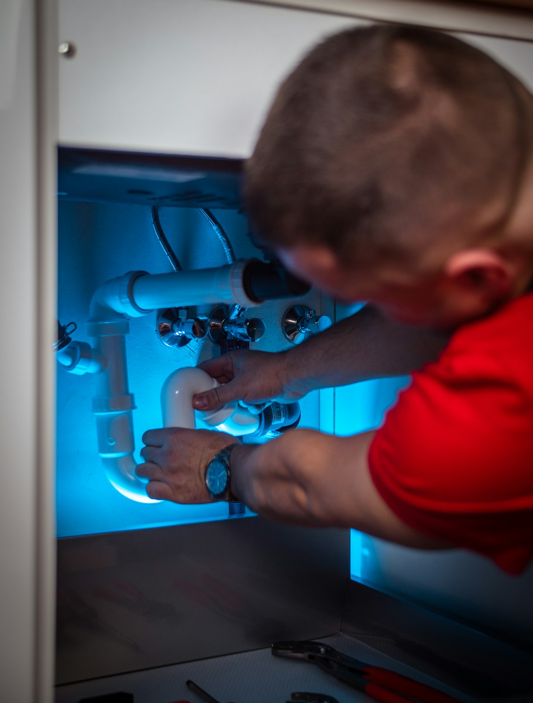 Plumber working on pipes under sink
