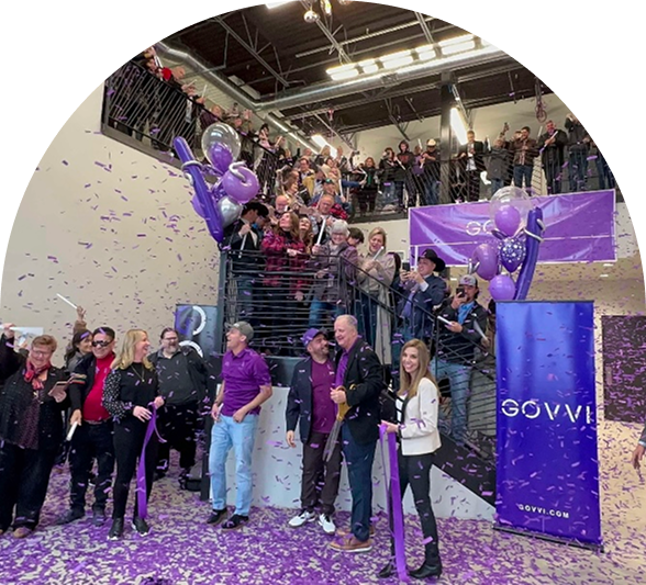 Group of people gathered at a stairway inside a building with purple confetti and balloons celebrating an event