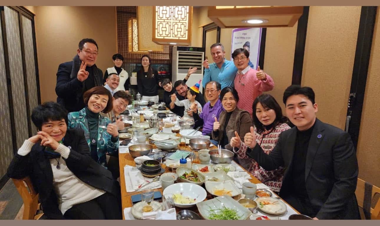 Group of people seated around a table at a restaurant, smiling and holding up one finger