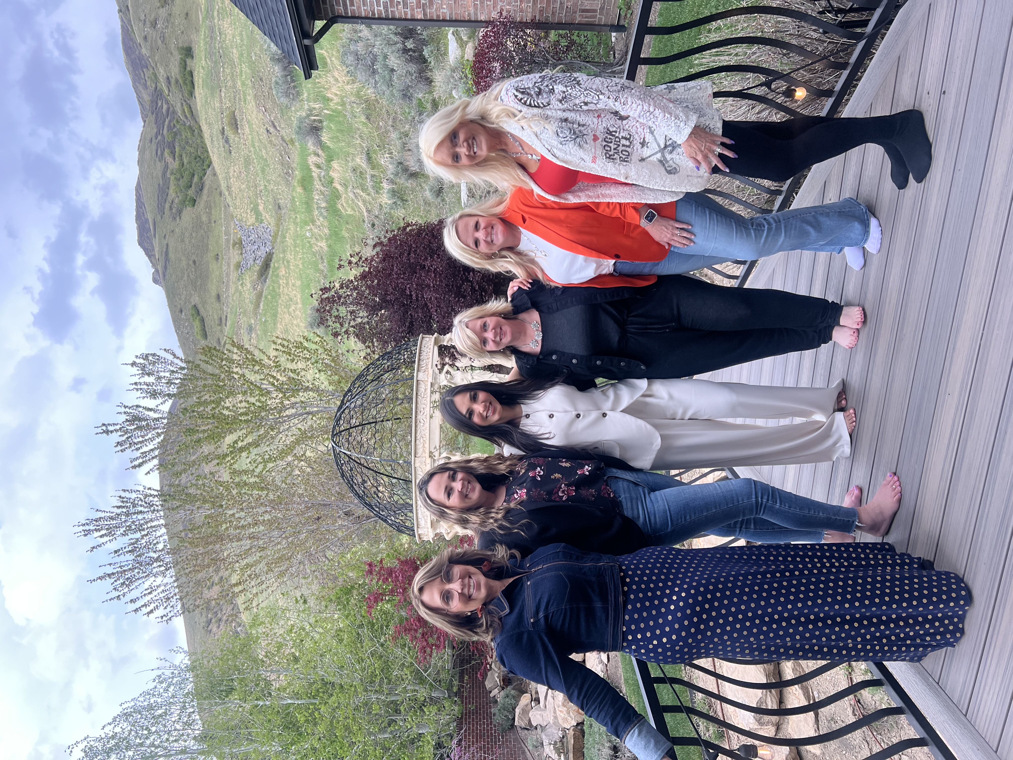 Group of women posing together on a wooden deck with a scenic view of hills and trees