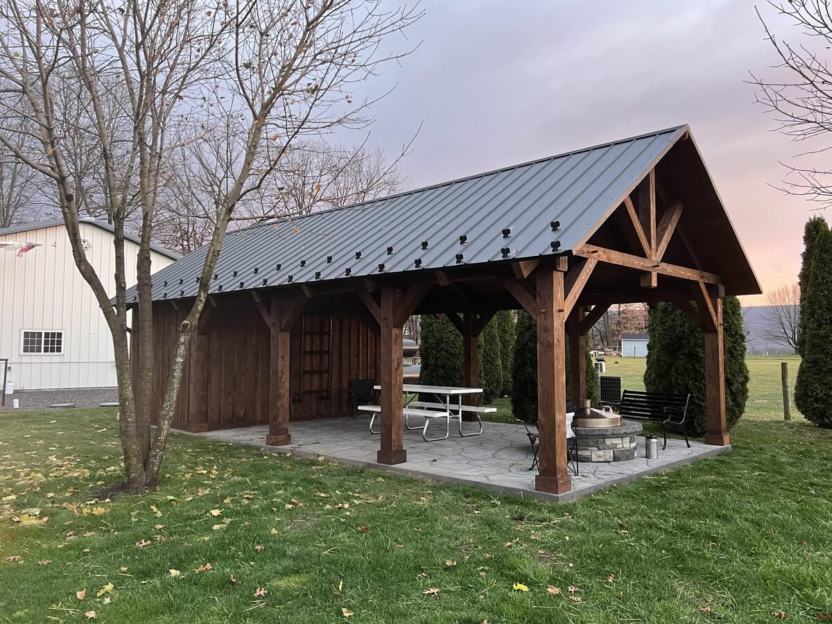 Timber-frame pavilion with standing-seam metal roof and stone fire pit