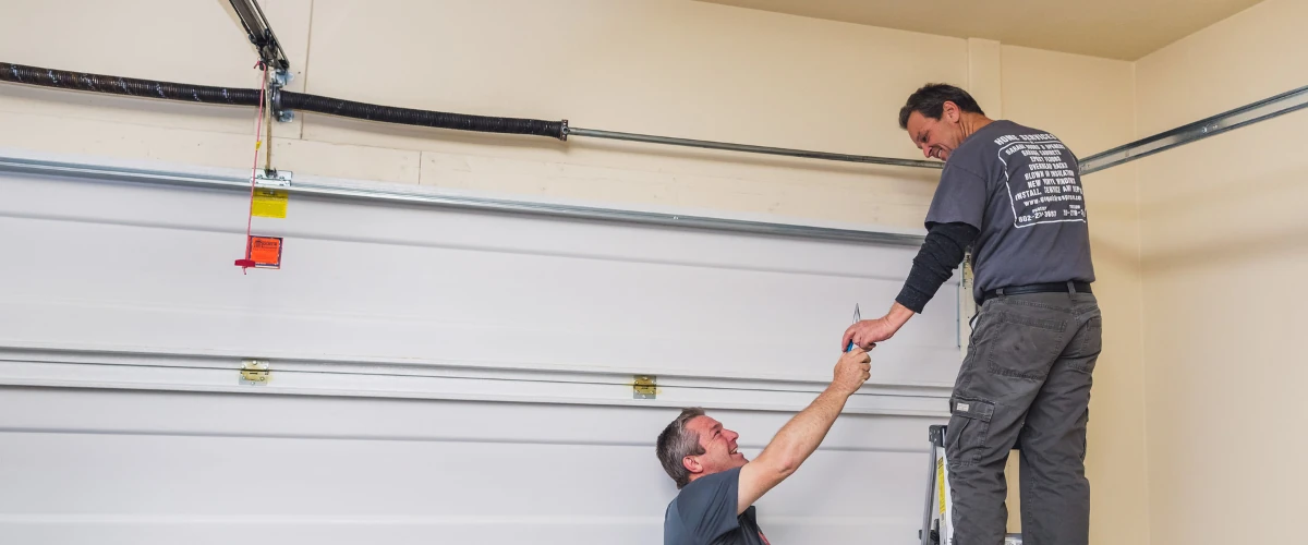 Garage door technicians working together to install and secure a residential garage door panel.