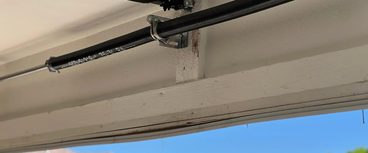 Garage door torsion spring bar and shaft assembly installed above a residential garage door.