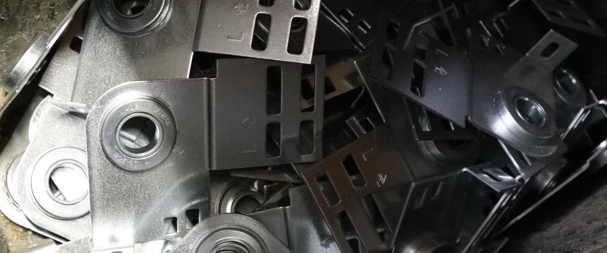 Close-up of a pile of shiny metallic mechanical assembly parts with bearings and slotted brackets.