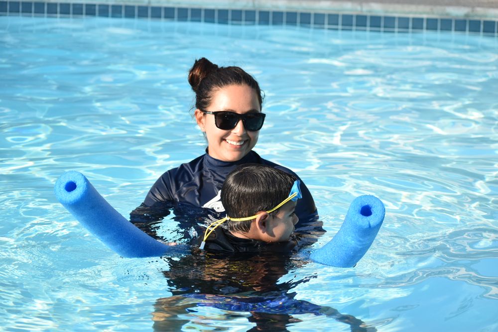 Instructor holding child with pool noodle, smiling brightly outdoors