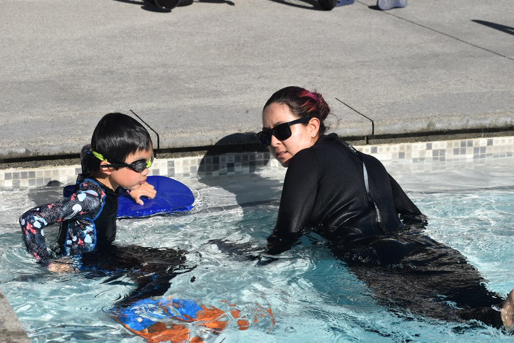 Child with floatation device at pool edge with instructor