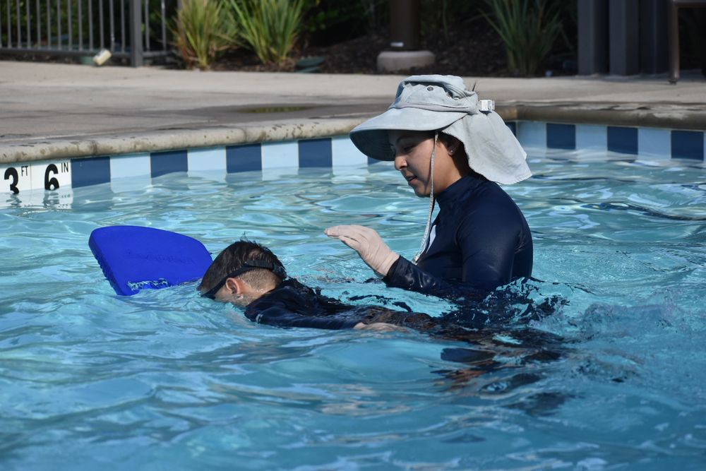 Instructor guiding child with kickboard in shallow pool