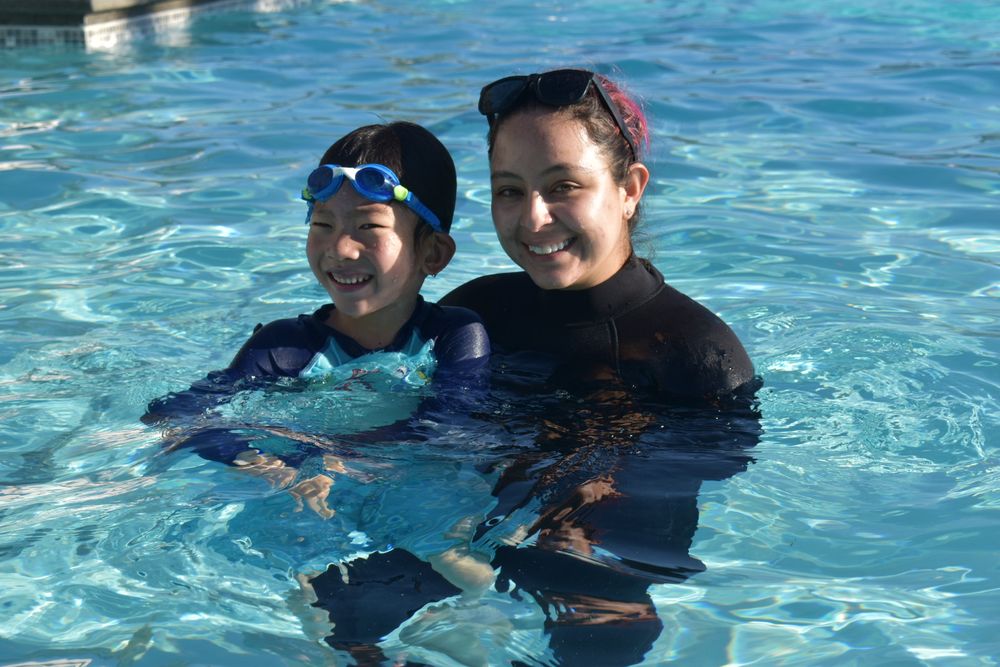 Coach Maria guiding a child in the pool during a one-on-one swim lesson