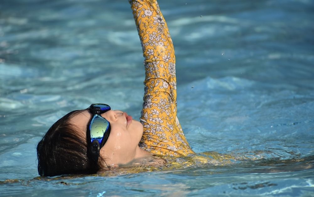Young swimmer in yellow floral swimsuit and goggles, relaxed and happy in the pool