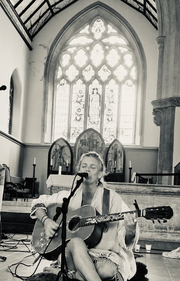Olivka singing into a microphone beneath a stained glass window.