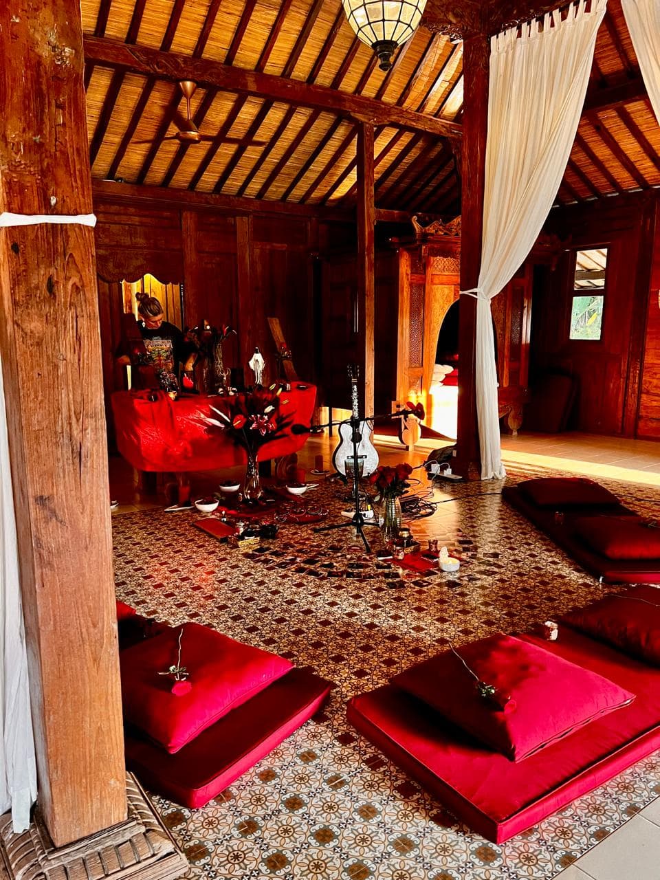The joglo set for ceremony, red cushions laid on the tiled floor around an altar and a guitar.