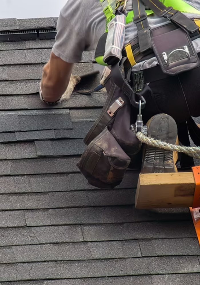 Construction worker wearing safety gear installing roof tiles on a residential roof.