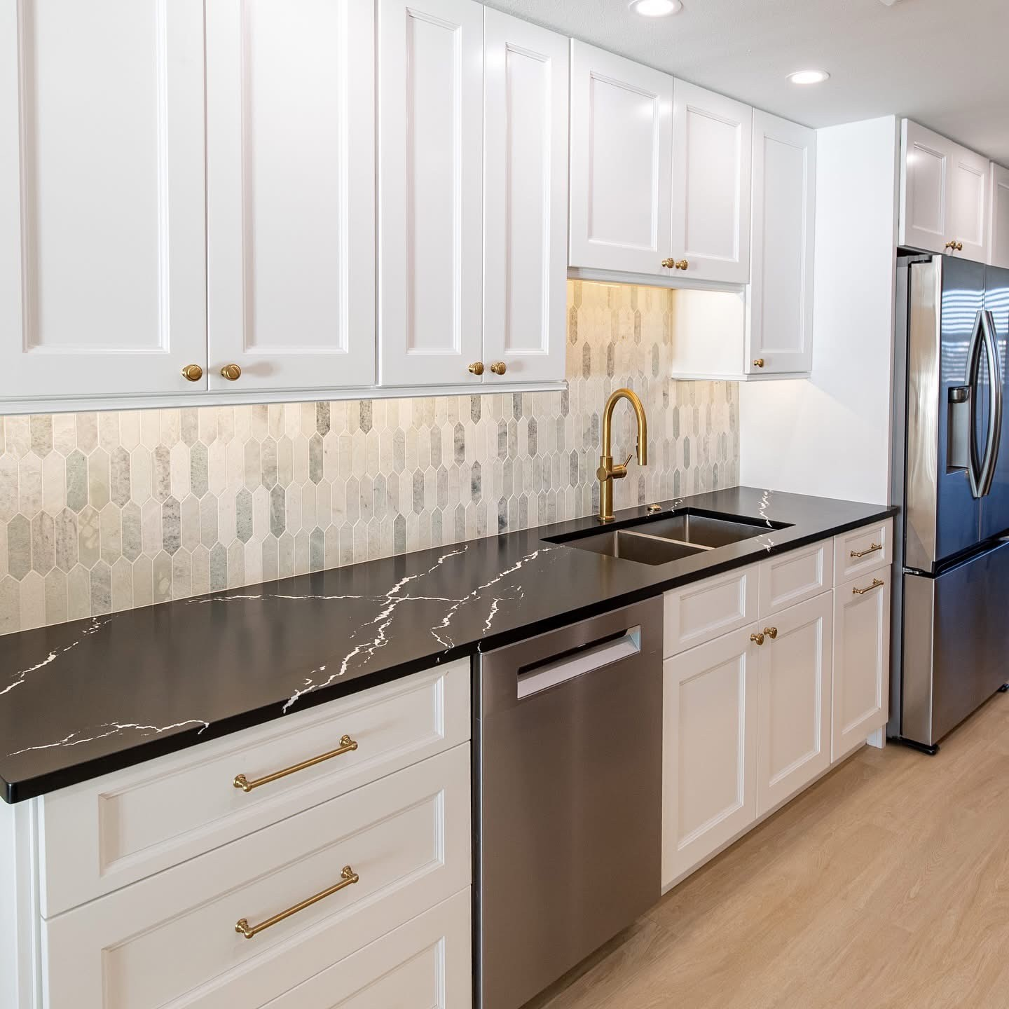 White kitchen with black countertop, brass faucet, and stainless steel appliances