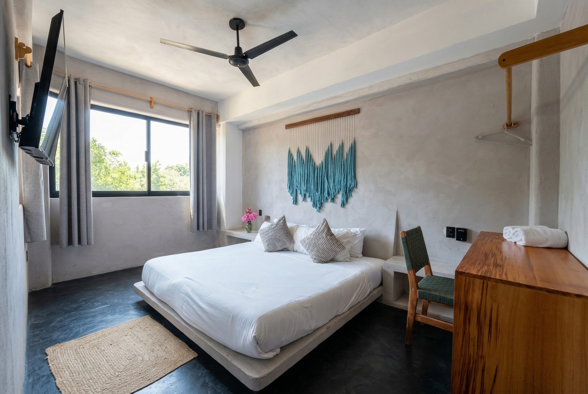 Bright bedroom with a king bed, turquoise macramé wall art, and garden views