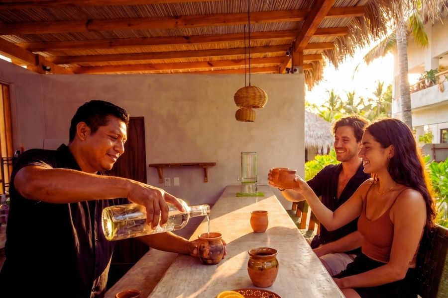 Bartender pouring artisanal mezcal at the poolside bar during golden hour at Casa Leah
