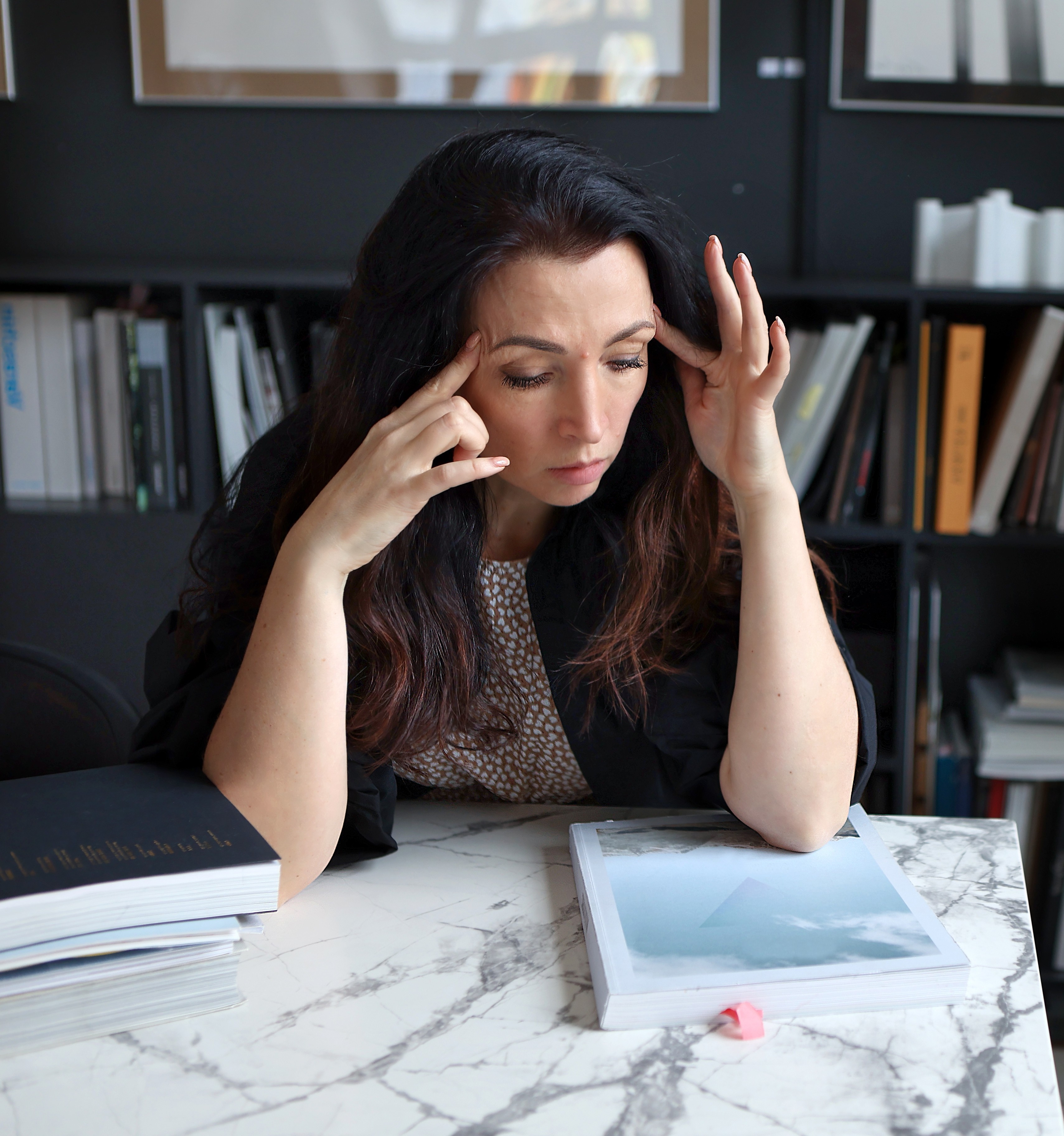 A practitioner at her desk with an open book, hands at her temples.