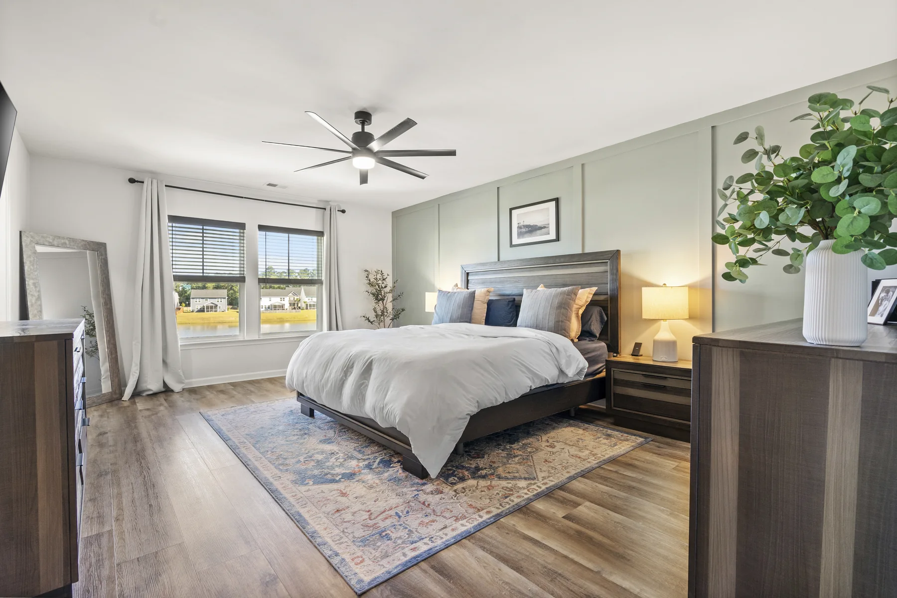Bedroom with a large bed, a ceiling fan, two windows, and a wall mirror