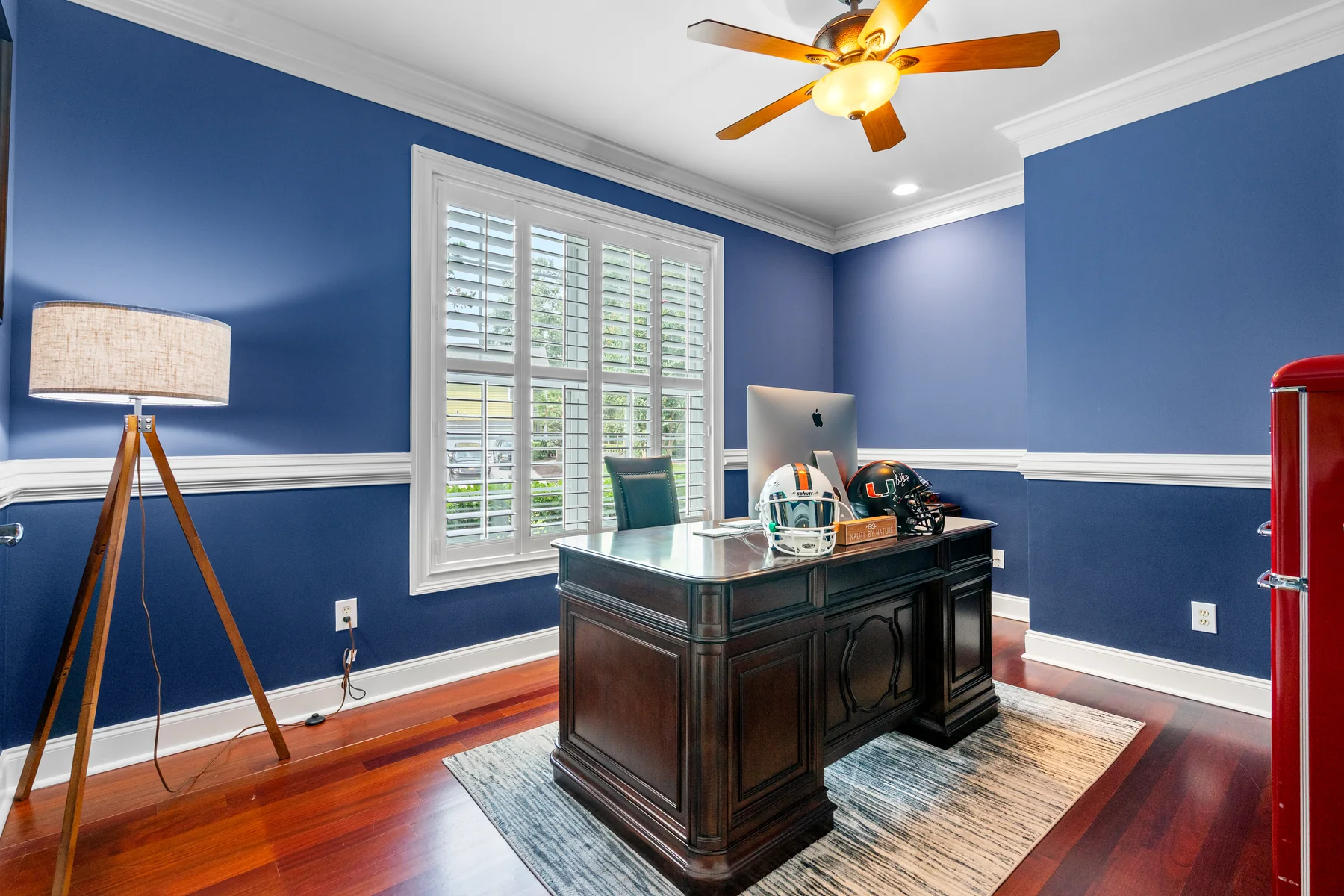 Home office with blue walls, a wooden desk, and a ceiling fan