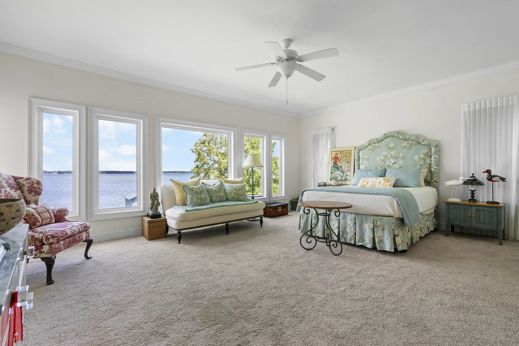 Bedroom with a bed, daybed, and chair beside windows with a lake view
